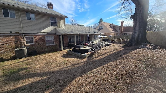 rear view of property with central air condition unit, a chimney, fence, and brick siding