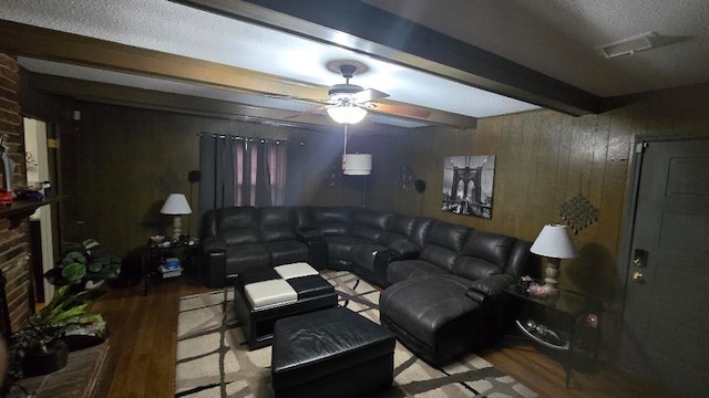 living area featuring ceiling fan, wood walls, wood finished floors, visible vents, and beamed ceiling