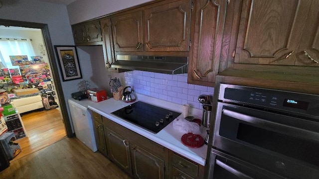 kitchen with under cabinet range hood, black electric stovetop, light countertops, and light wood finished floors