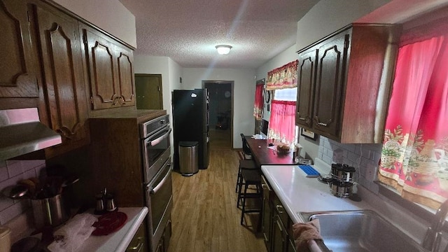 kitchen with light wood finished floors, decorative backsplash, freestanding refrigerator, a textured ceiling, and under cabinet range hood