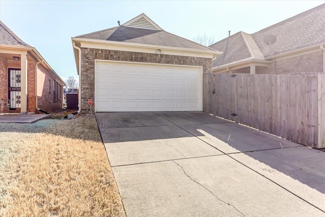 exterior space with brick siding, a shingled roof, fence, a garage, and driveway