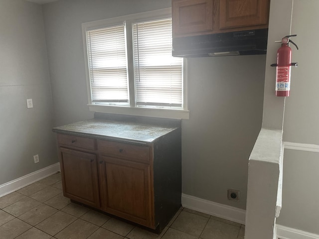 kitchen featuring baseboards, light countertops, light tile patterned flooring, and range hood