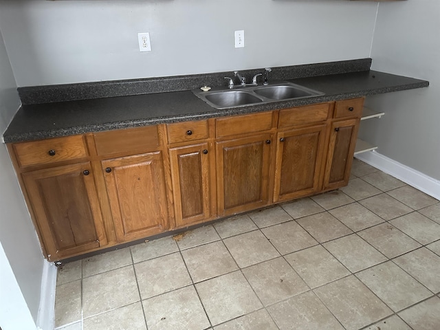 kitchen with light tile patterned floors, dark countertops, a sink, and brown cabinets