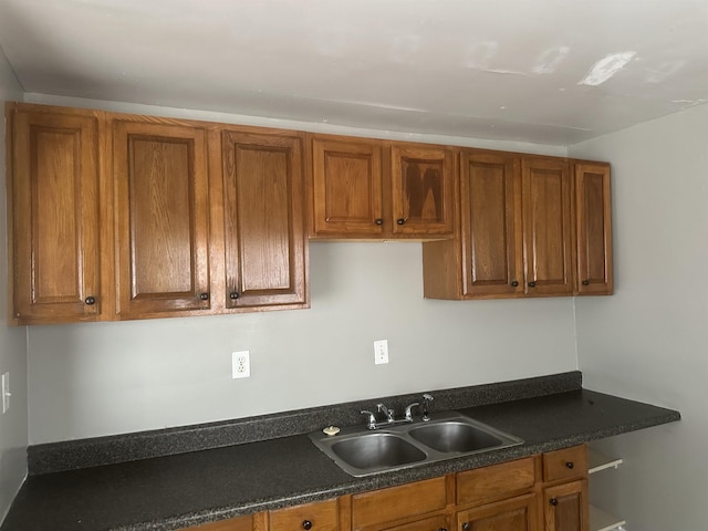 kitchen with brown cabinetry, dark countertops, and a sink