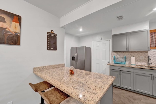 kitchen featuring tasteful backsplash, visible vents, stainless steel fridge with ice dispenser, gray cabinetry, and a sink