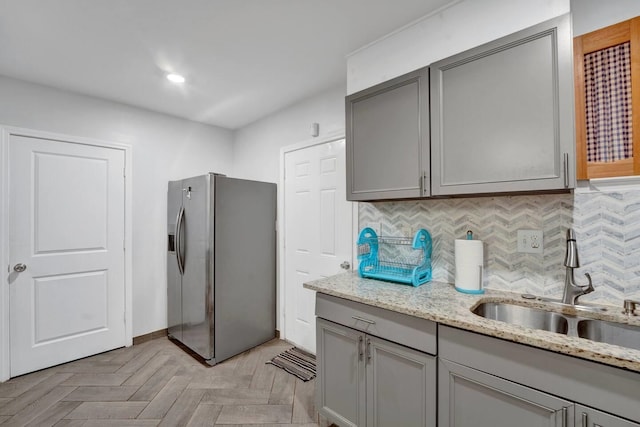 kitchen featuring backsplash, stainless steel fridge, gray cabinets, and a sink