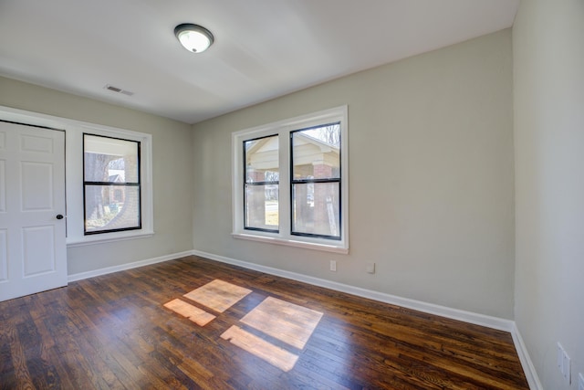 empty room with baseboards, visible vents, and dark wood-type flooring