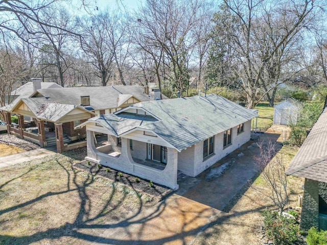 view of front of house featuring an outbuilding, brick siding, a chimney, a shed, and driveway