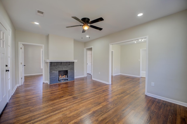 unfurnished living room featuring baseboards, visible vents, dark wood finished floors, a ceiling fan, and a brick fireplace