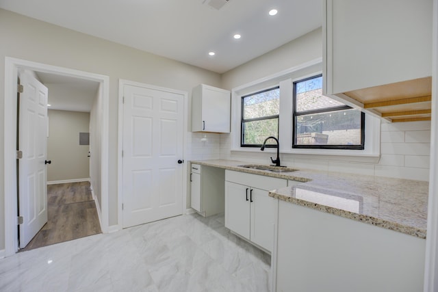 kitchen with tasteful backsplash, white cabinets, light stone countertops, marble finish floor, and a sink