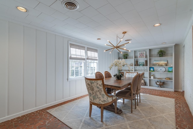 dining space featuring built in features, a notable chandelier, visible vents, a decorative wall, and ornamental molding