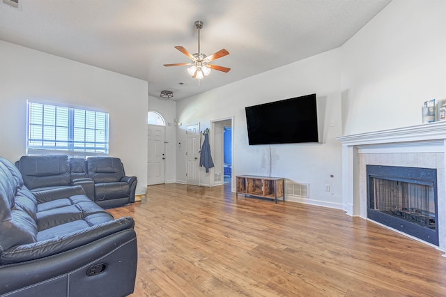 living area featuring visible vents, light wood-style floors, a ceiling fan, a tile fireplace, and baseboards