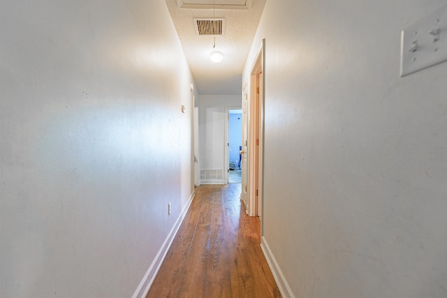 hall featuring attic access, visible vents, baseboards, and wood finished floors