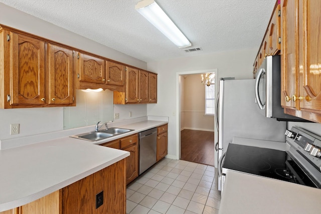 kitchen with stainless steel appliances, brown cabinetry, visible vents, and a sink