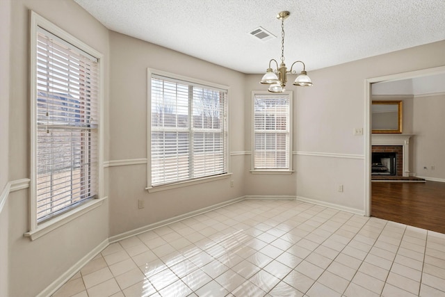 unfurnished dining area with a brick fireplace, tile patterned flooring, visible vents, and an inviting chandelier