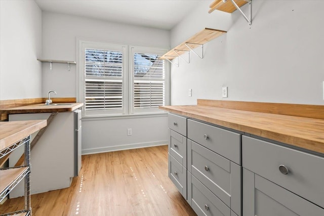 kitchen featuring baseboards, butcher block countertops, gray cabinets, light wood-type flooring, and a sink