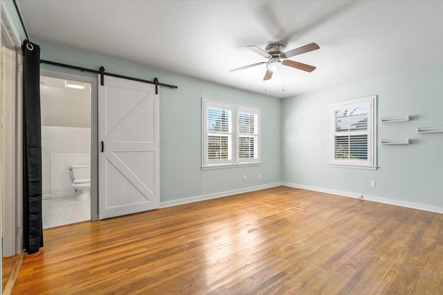 interior space featuring ceiling fan, a barn door, wood finished floors, and baseboards