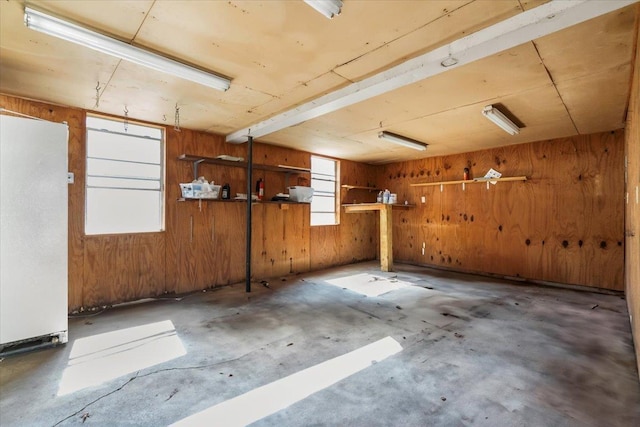 basement with a garage, freestanding refrigerator, and wood walls