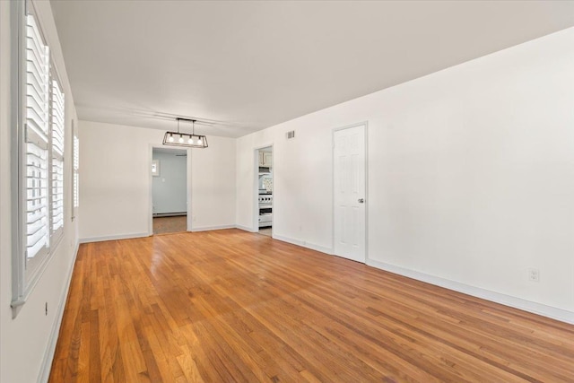 spare room with light wood finished floors, visible vents, baseboards, a baseboard radiator, and a notable chandelier