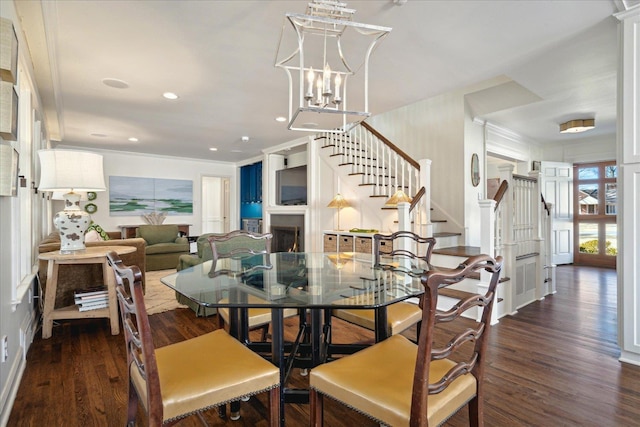 dining area with a warm lit fireplace, recessed lighting, wood finished floors, ornamental molding, and stairway