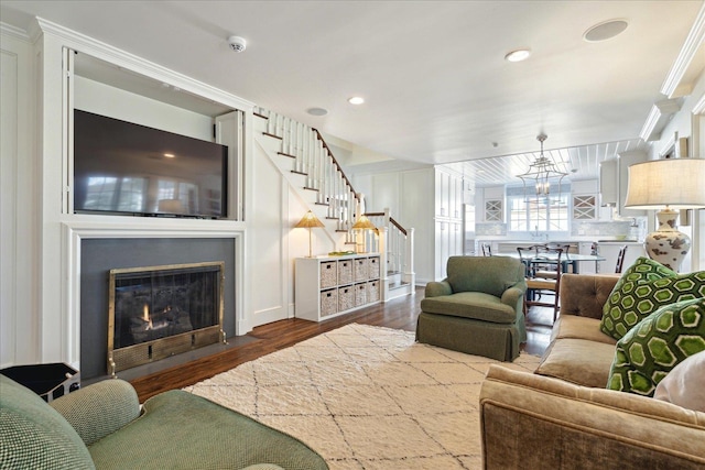 living area with recessed lighting, a fireplace with flush hearth, wood finished floors, stairway, and crown molding