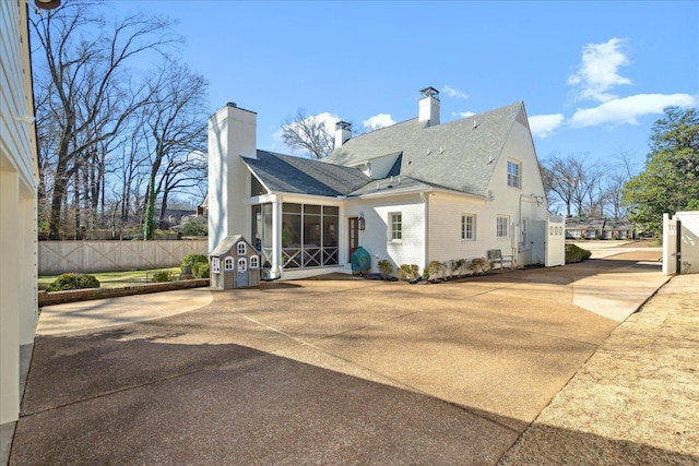 rear view of property featuring brick siding, roof with shingles, a chimney, a sunroom, and fence