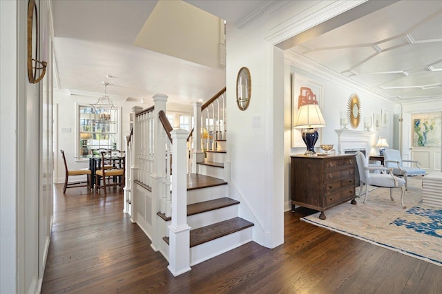 stairway with baseboards, hardwood / wood-style floors, crown molding, a fireplace, and a notable chandelier