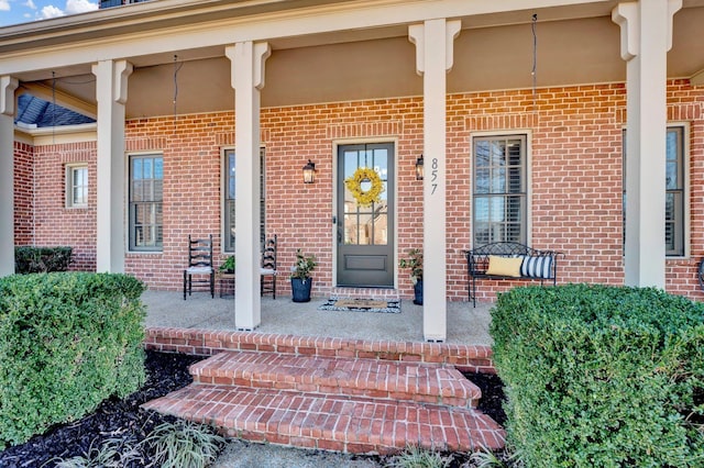 entrance to property featuring a porch and brick siding