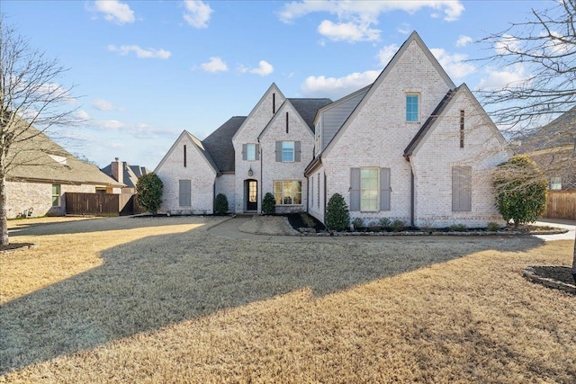 french country style house featuring brick siding, fence, and a front lawn