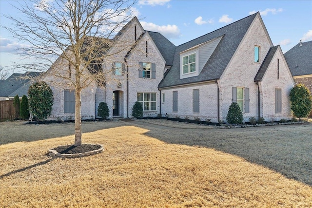 french country style house featuring brick siding, a front lawn, and fence