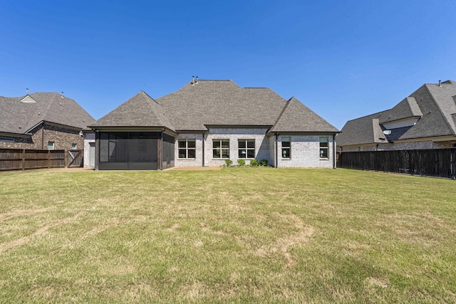 rear view of property featuring a sunroom, a shingled roof, a fenced backyard, and a lawn