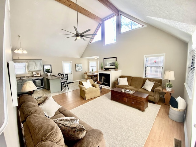 living room with a ceiling fan, light wood-type flooring, beam ceiling, and visible vents