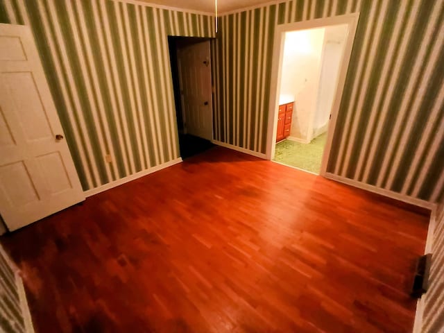 empty room featuring wallpapered walls, baseboards, and wood finished floors