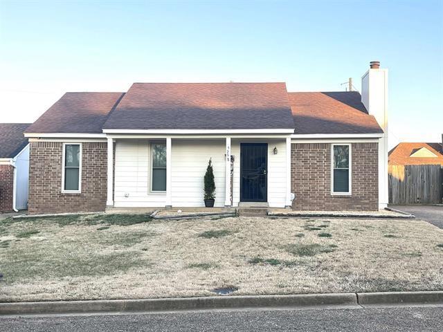 ranch-style home with brick siding, a shingled roof, fence, a chimney, and a front yard