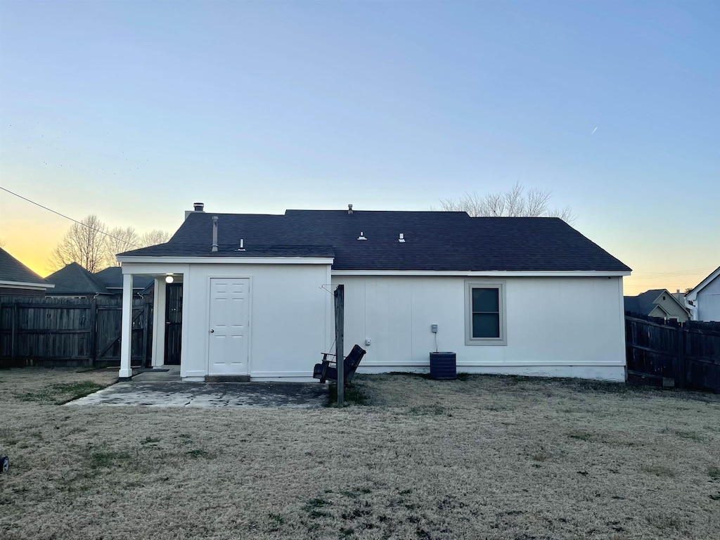 back of property at dusk featuring central AC unit, fence, and a lawn