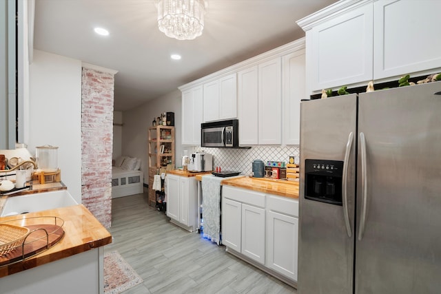 kitchen with stainless steel appliances, wooden counters, decorative backsplash, white cabinets, and a chandelier