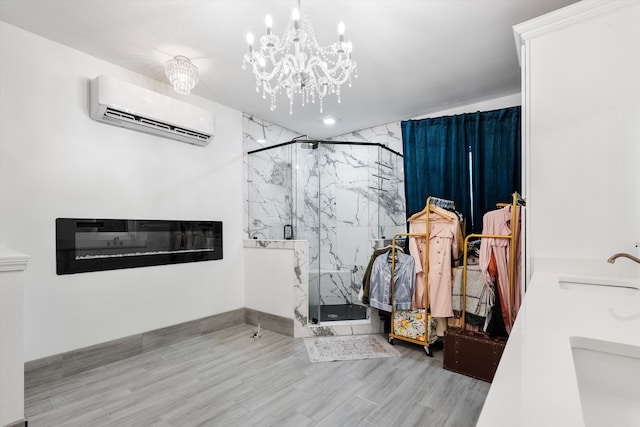 full bath with a marble finish shower, a wall mounted AC, a sink, wood finished floors, and a chandelier