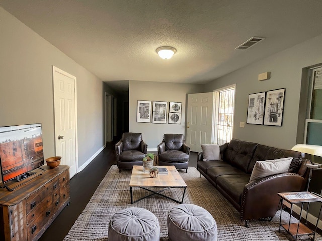 living area featuring a textured ceiling, wood finished floors, visible vents, and baseboards