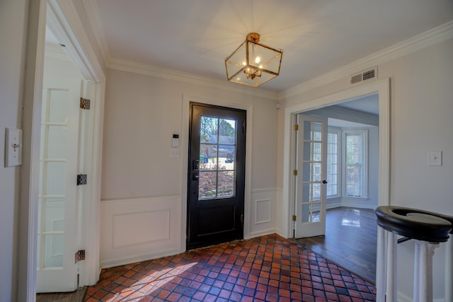 entryway with visible vents, a wainscoted wall, dark wood-type flooring, crown molding, and a notable chandelier