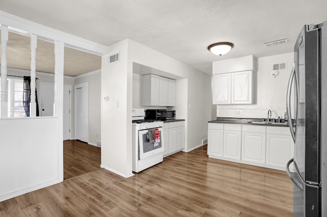 kitchen featuring white gas range oven, a sink, freestanding refrigerator, and white cabinets