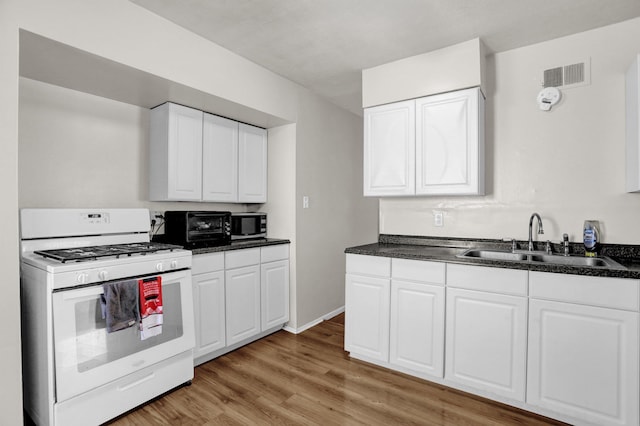 kitchen with white gas range, dark countertops, visible vents, stainless steel microwave, and a sink