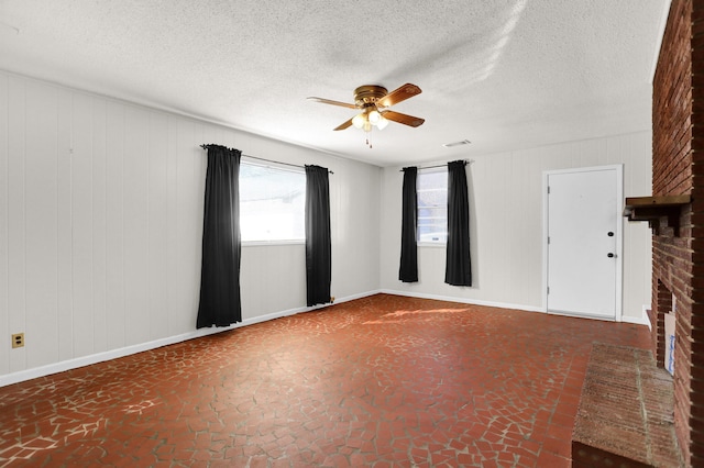 unfurnished room with visible vents, baseboards, ceiling fan, a textured ceiling, and a brick fireplace