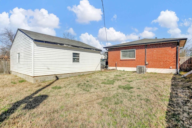 rear view of house featuring a yard, brick siding, central AC, and fence