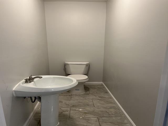 half bathroom with toilet, marble finish floor, and baseboards