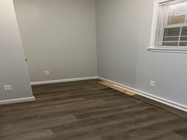 unfurnished room with baseboards and dark wood-type flooring