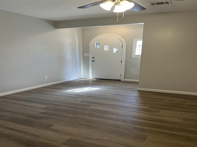 foyer entrance with arched walkways, ceiling fan, dark wood-type flooring, and baseboards