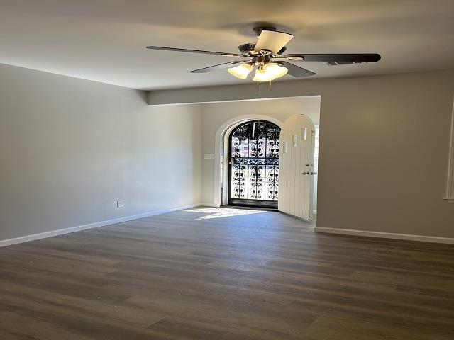 empty room with dark wood-style floors, ceiling fan, and baseboards