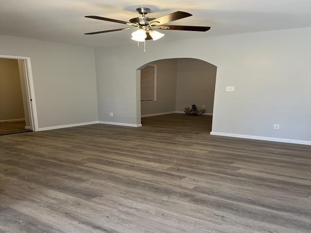 empty room with arched walkways, baseboards, and wood finished floors