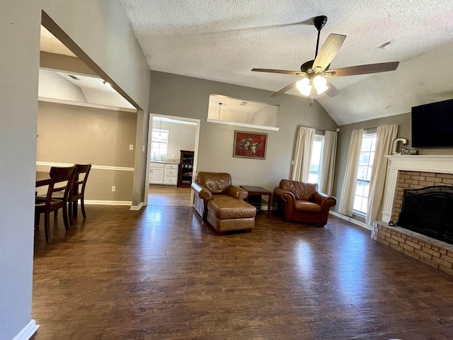 living room with ceiling fan, a brick fireplace, vaulted ceiling, and wood finished floors