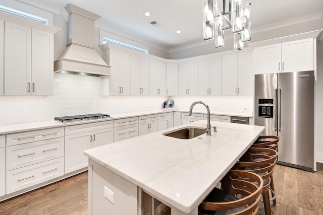 kitchen featuring gas stovetop, a sink, light wood-type flooring, premium range hood, and high end refrigerator